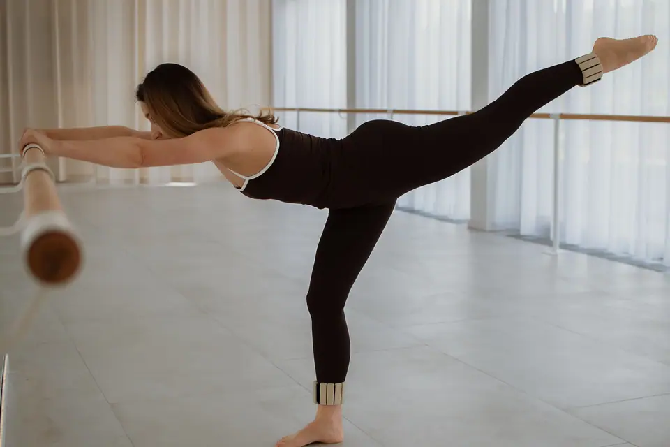 Arabesque an der Ballettstange: ein Bein gestreckt nach hinten, die Arme lang, vor der hellen Fensterfront