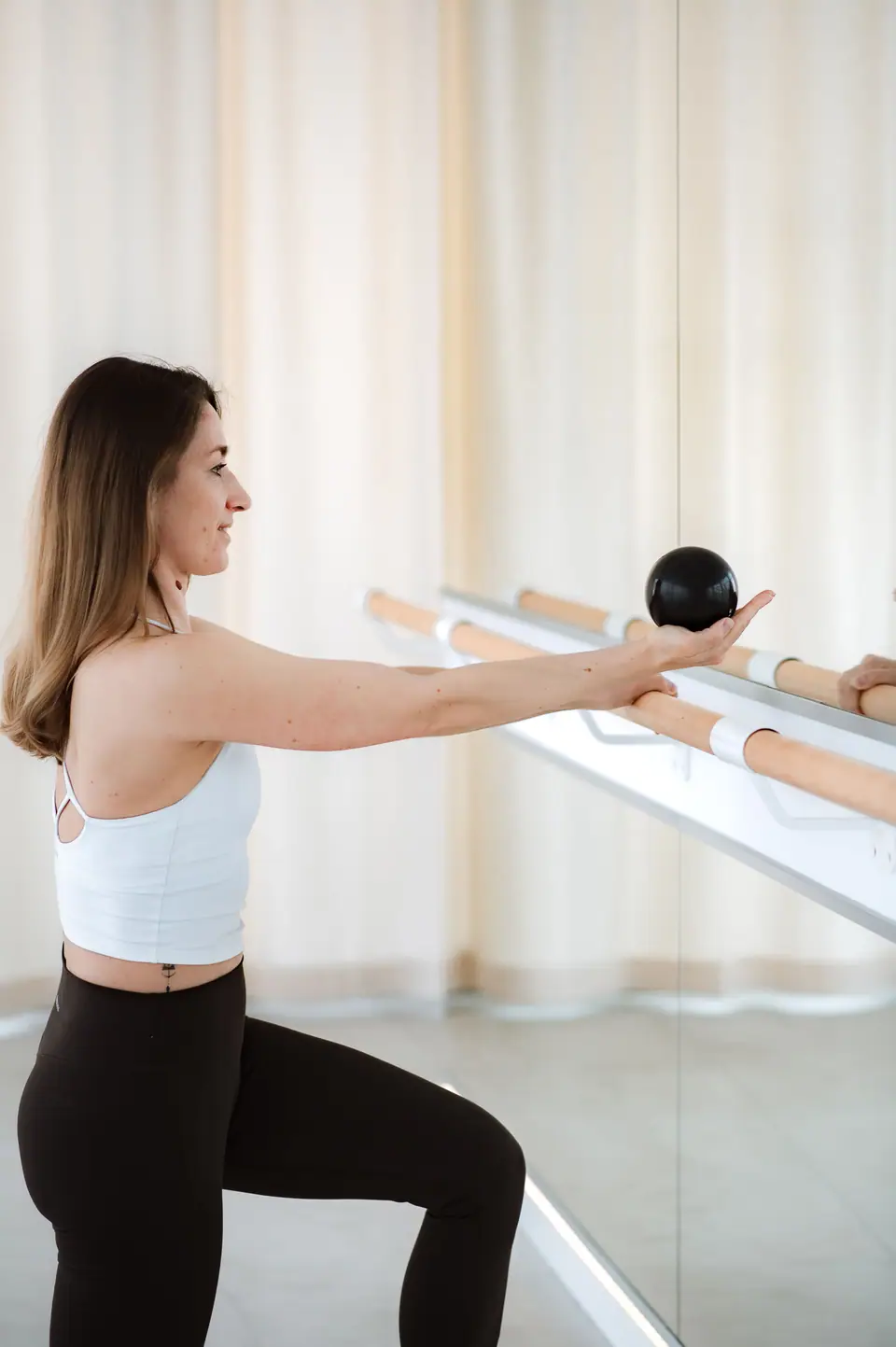 Barre-Übung mit kleinem Ball: Anastasija Berg reicht den Ball über die Ballettstange, die Knie leicht gebeugt
