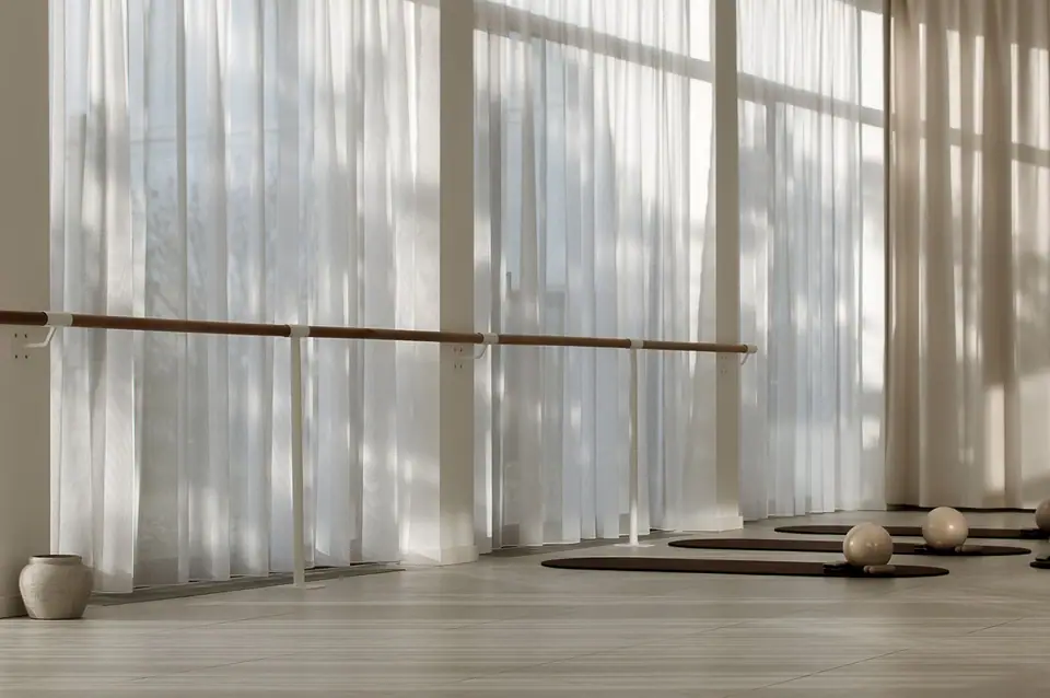 Lichtdurchfluteter Trainingsraum mit Vorhängen, Ballettstange und Matten im MÉ·US Studio