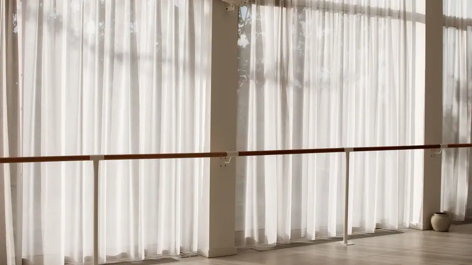 Ballettstange vor der Fensterfront im MÉ·US Studio, warmes Licht durch die Vorhänge