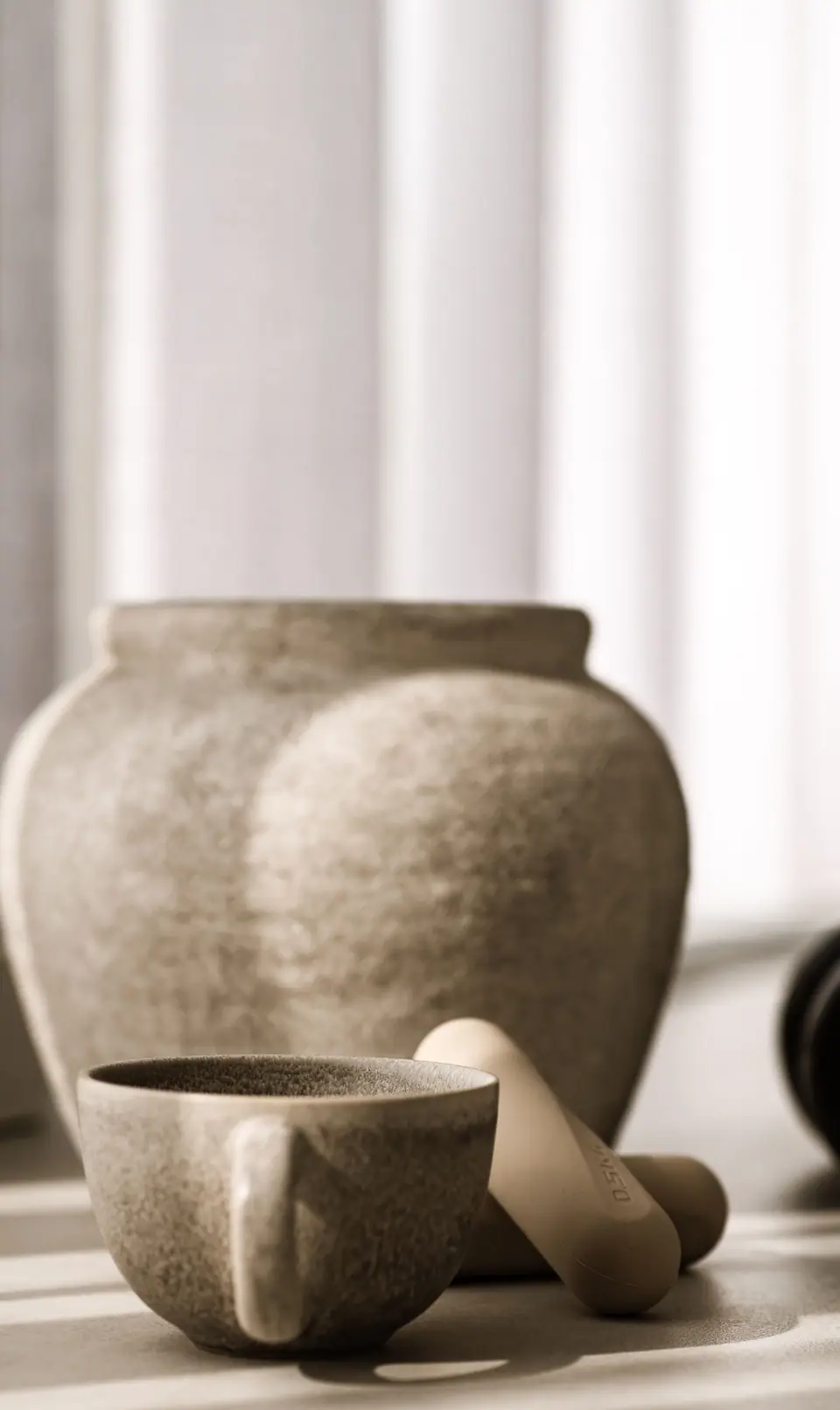 Keramiktasse, Tonvase und Pilates-Griffe im warmen Licht vor den Vorhängen des MÉ·US Studios