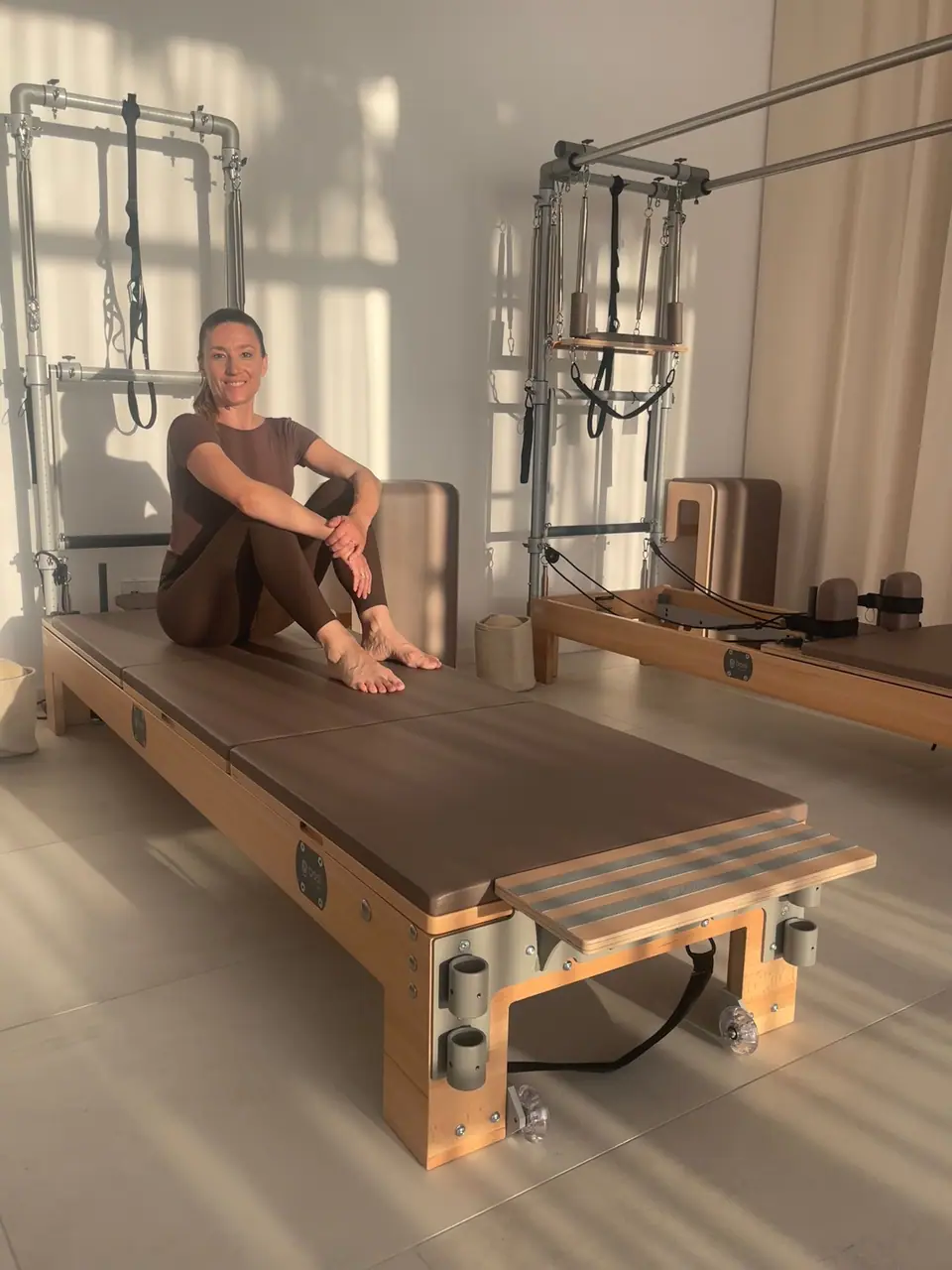 Anastasija Berg sitzt auf dem Reformer zwischen den BASI Geräten im MÉ·US Studio